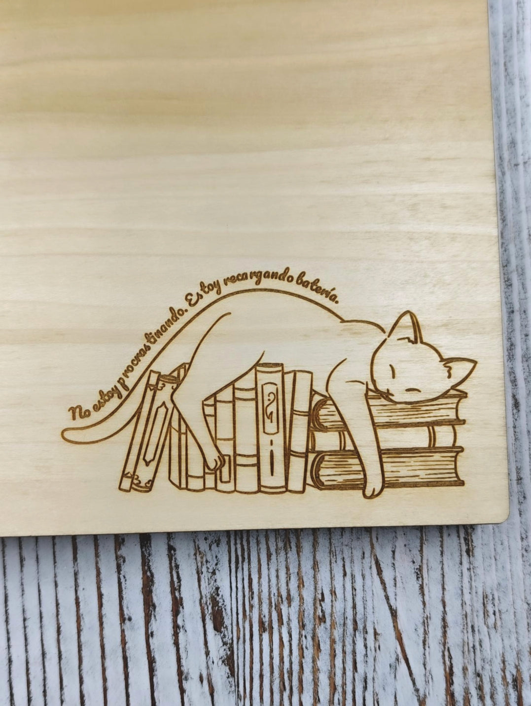Detalle de gato dormido sobre libros grabado en madera, frase No estoy procrastinando