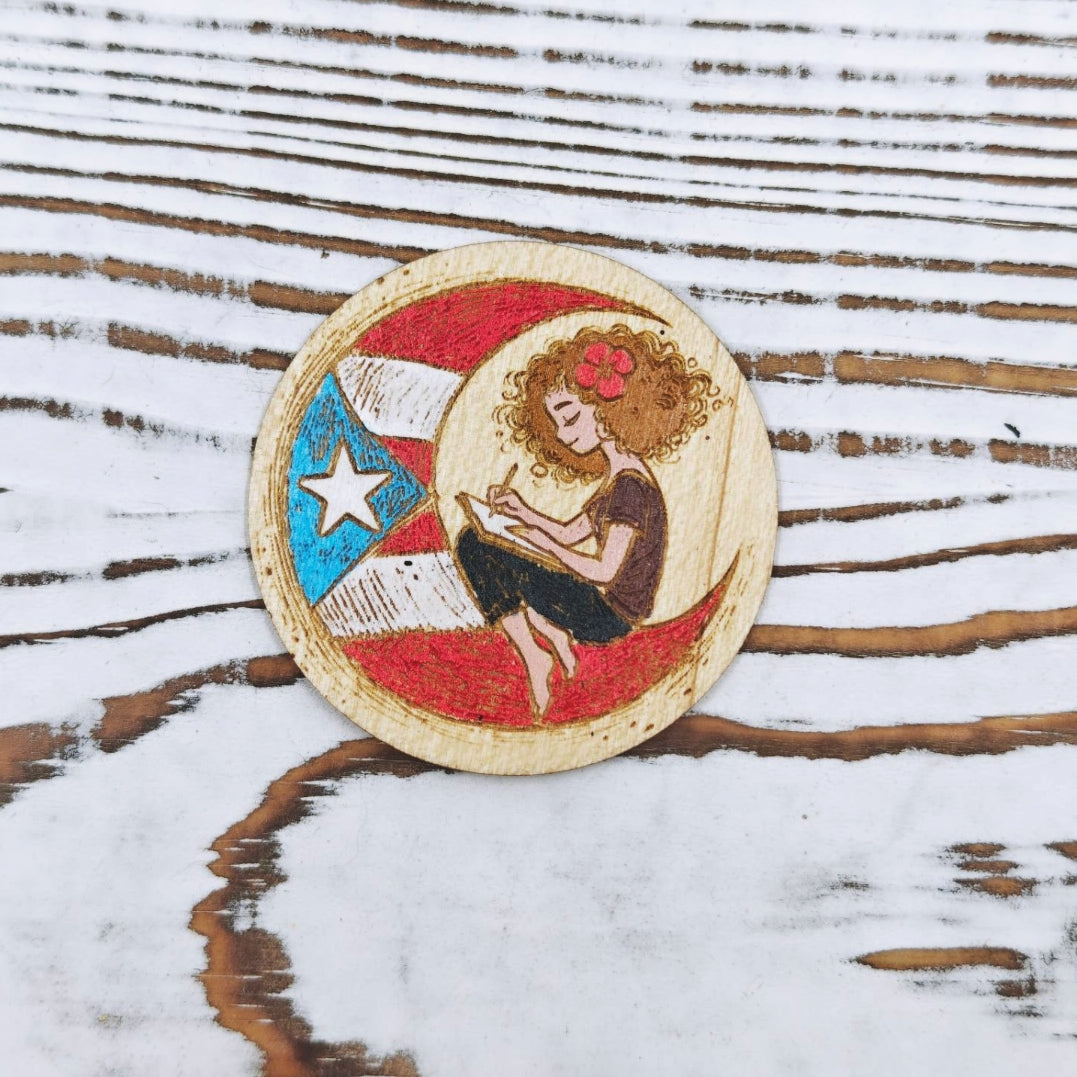 Sticker de madera de arce inspirado en el poema "Boricua en la Luna", con ilustración de una joven escribiendo sobre la bandera de Puerto Rico, pintado a mano.